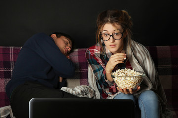 Lovely girl watching a movie, and her friend is sleeping on a sofa.