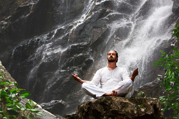 Man sitting in meditation yoga on rock at waterfall in tropical - obrazy, fototapety, plakaty