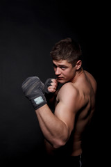 Fototapeta na wymiar Muscular athletic man boxing on a black background. A man with a naked torso in shorts, hands peremotanye bandages for boxing.