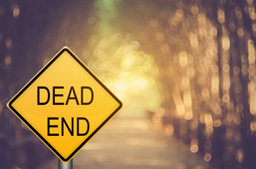 Dead end warning sign on blur traffic road with colorful bokeh light abstract background.
