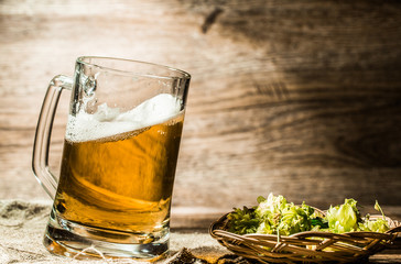 Beer mug stands on table next to hop in basket