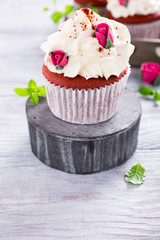 Delicious red velvet cupcakes decorated with pink rose on old white wooden background. Valentines Day dessert. Copy space.