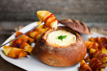 Tasty hot cheese fondue served in a bread roll with potatoes and