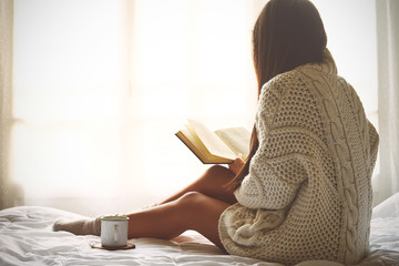 Young woman sitting in bed while reading a book