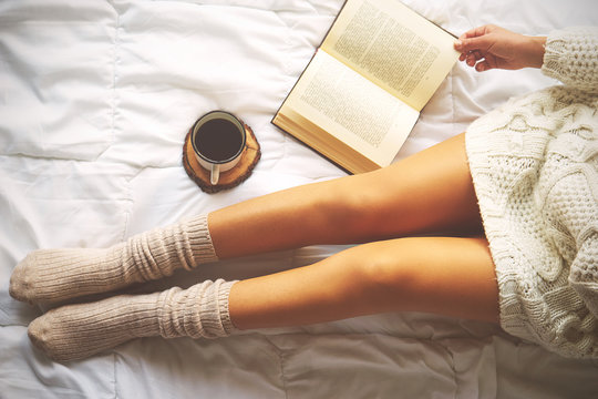 Soft photo of woman on the bed with book and cup of coffee, top view