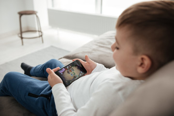 Side view photo of boy holding smartphone and playing game