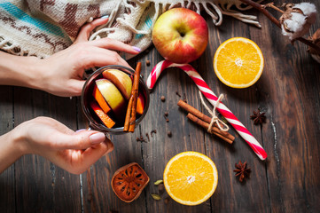 Female hands holding a hot mulled wine with spices, apple and or