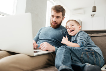 Cheerful father using laptop computer with his little cute son.