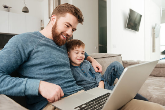 Joyful father using laptop computer with his little cute son.