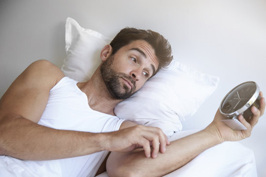 Sleepy man holding alarm clock in bed