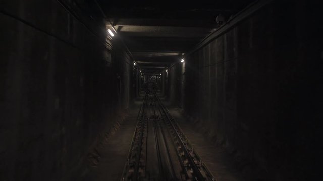 Pov view from small funicular wagonette moving through narrow undegraound tunnel in mountains uphill and meeting other train descending to down station. Warm dimmed lights on walls