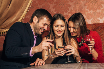two cute women and a man sitting in  restaurant  use the phone