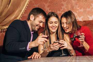 two cute women and a man sitting in  restaurant  use the phone