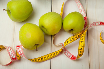 Green apples with measuring tape on a white wooden table