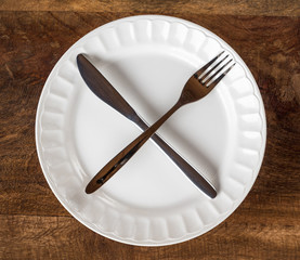 Intermittent fasting concept with knife and fork showing cross symbol on white plate against wooden...