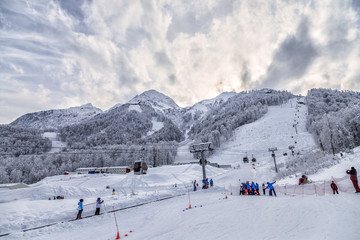 Fototapeta na wymiar Snowy ski tracks and cableway ski lifts in Sochi winter mountain ski resort. Beautiful scenic landscape with snow covered peaks at sunset