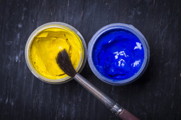 Blue and yellow paint with brush on white black wooden background. Set for the artist. Education.