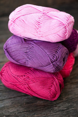 Different types of pink and purple yarn on a wooden background