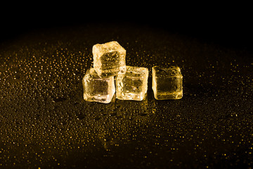Ice cubes in yellow light on black wet table.