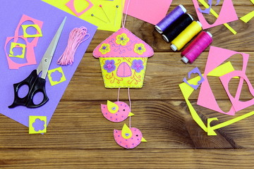 Obraz premium Homemade bright house with flowers and birds made of felt. Beautiful wall decor, sewing materials and tools on wooden table. Fun sewing craft concept. Simple spring or summer crafts for kids. Top view