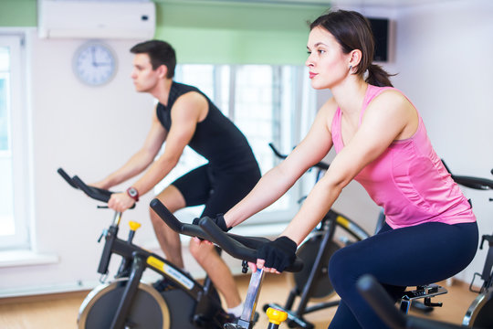 Group training people biking in the gym, exercising legs doing cardio workout cycling bikes