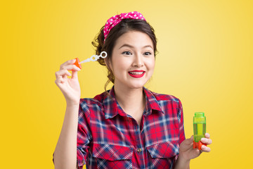 Pinup model blowing soap bubbles over yellow background.