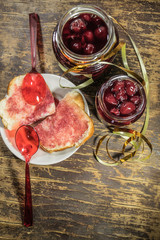 Cherry jam and white bread on wooden background