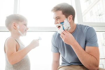 Cute father and son are applying shaving foam in bathroom