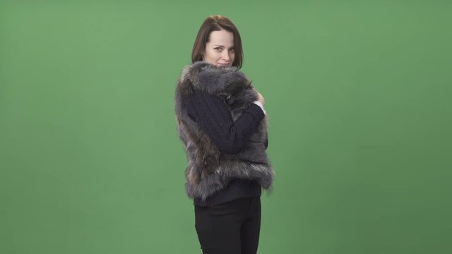 Young brunette woman demonstrating fur vest  against chroma key green screen background