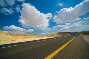 Asphalt road in the Judean desert on a background of blue sky with clouds