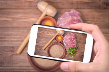 Hands taking photo raw pork schnitzel   with smartphone.