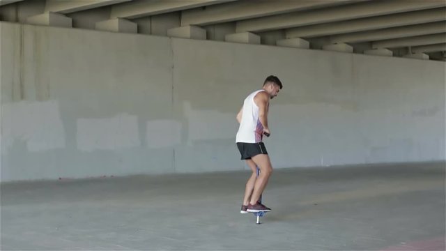 Slow motion. Sports guy in a white t-shirt and shorts jumping on the spring device under a bridge.