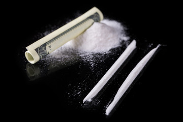 Rolled hundred dollars banknote and two lines of cocaine on blac