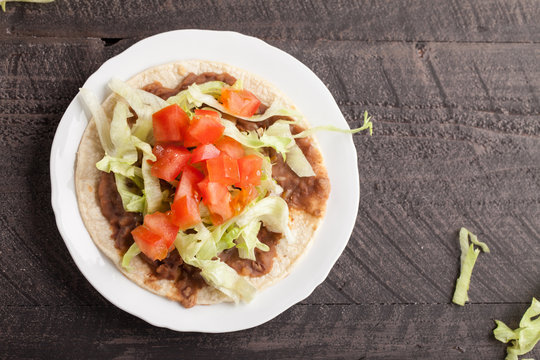 Corn tortilla tostada with refried beans, lettuce, salsa, and tomatoes horizontal top view