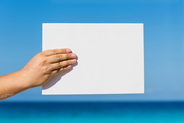 Blank white board in hand against beach view background