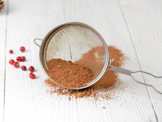 Cocoa powder in a sieve isolated on white wooden background