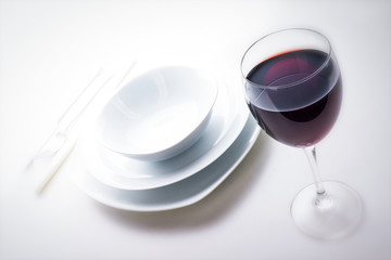 Rotwein im Glas mit Geschirr Besteck und Servette auf weißem Tisch, Hintergrund