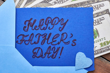 Dollars near Father's Day card. Blue fabric heart on card. Financial support for dad.