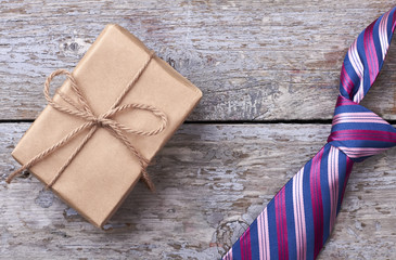 Obraz premium Gift box near striped necktie. Tie on wooden surface. How to choose a present.