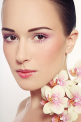Close-up portrait of young beautiful healthy woman with fresh make-up and white orchid