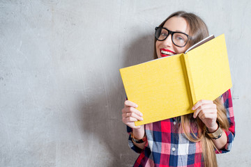 Portrait of a young happy student in checkered shirt with yellow book on the gray wall background