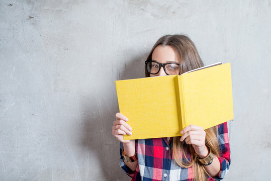 Portrait of a young happy student in checkered shirt with yellow book on the gray wall background