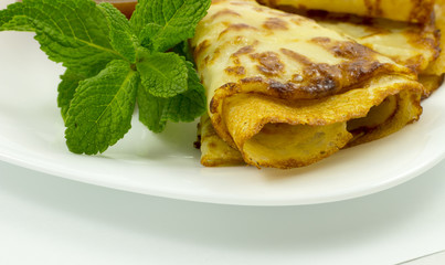 Crepes on a white plate with mint leaves and a Cup of honey