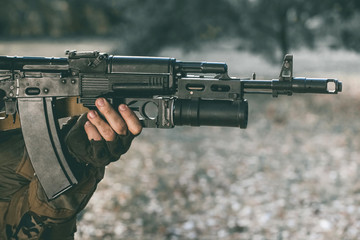 The soldier in the performance of tasks in camouflage and protective gloves holding a gun. War Zone.