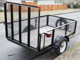 Empty two-wheel trailer with wire mesh sides parked on residential neighborhood street.