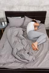 Young tired man in pajama sleeping without blanket in stylish be