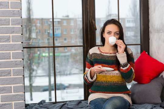 Young woman drinking coffee while sitting on windowsill