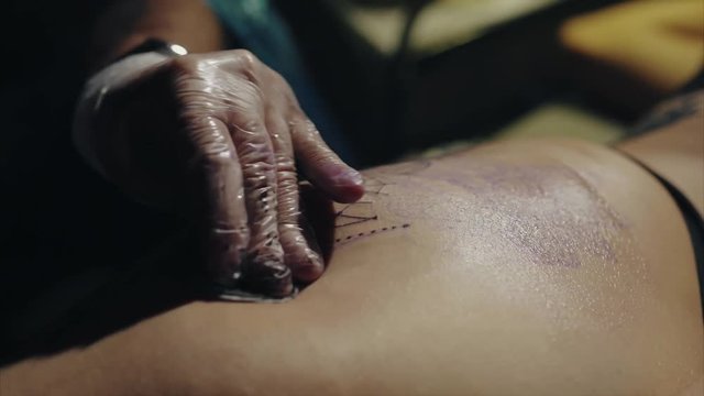 Close-up of hands of tattoo artist in gloves tattooing a pattern on body macro 4K