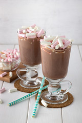 Cocoa drink with mini marshmallows in two glasses on white wooden table.