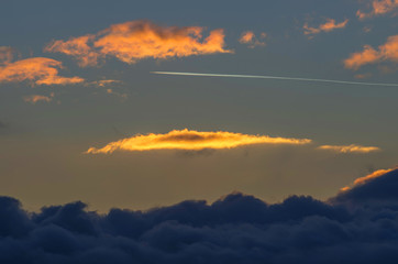 Jet plane with reverse jet flying above the clouds at sunset.